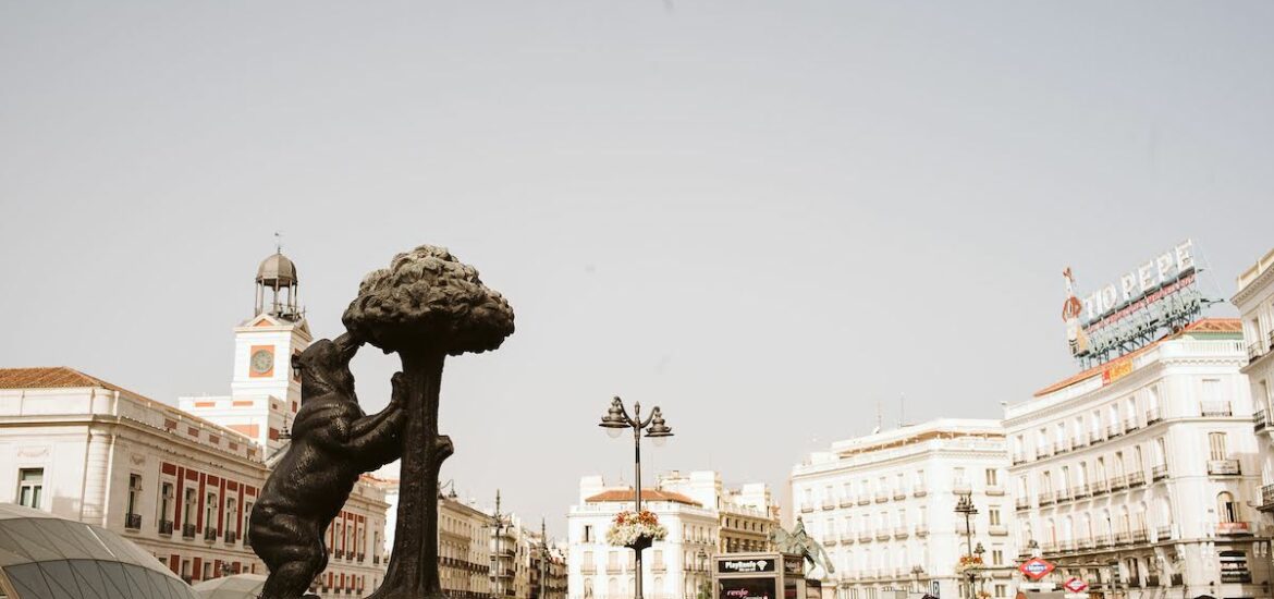 Busy city plaza with a statue of a bear eating from a strawberry tree in the foreground.