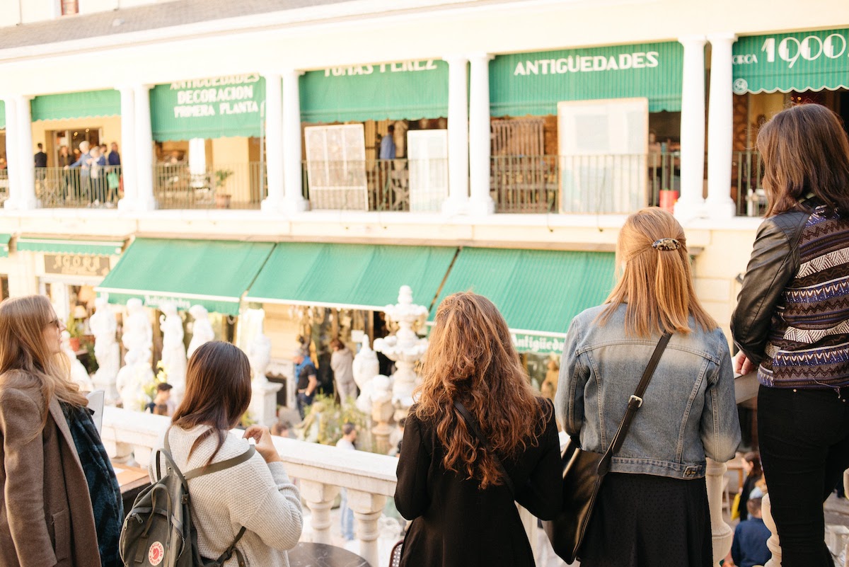 Group of people from behind facing storefronts with green awnings.