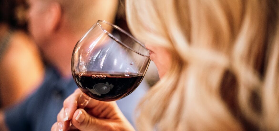 A blond woman smelling a glass of red wine