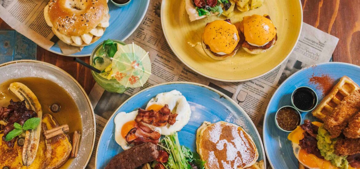 various colorful plates with breakfast spreads such as eggs, wafffles, and bagels