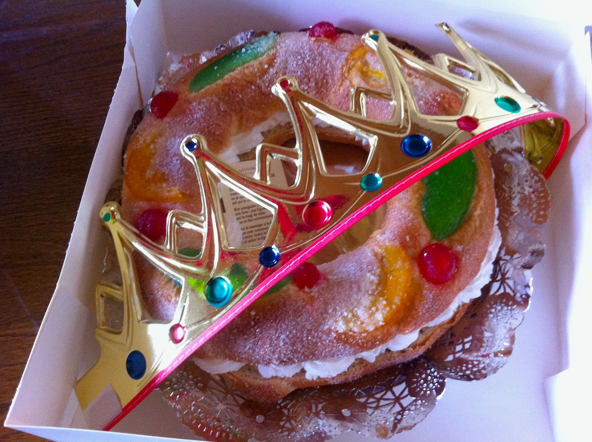 A round cream-filled cake in a box with a paper crown.