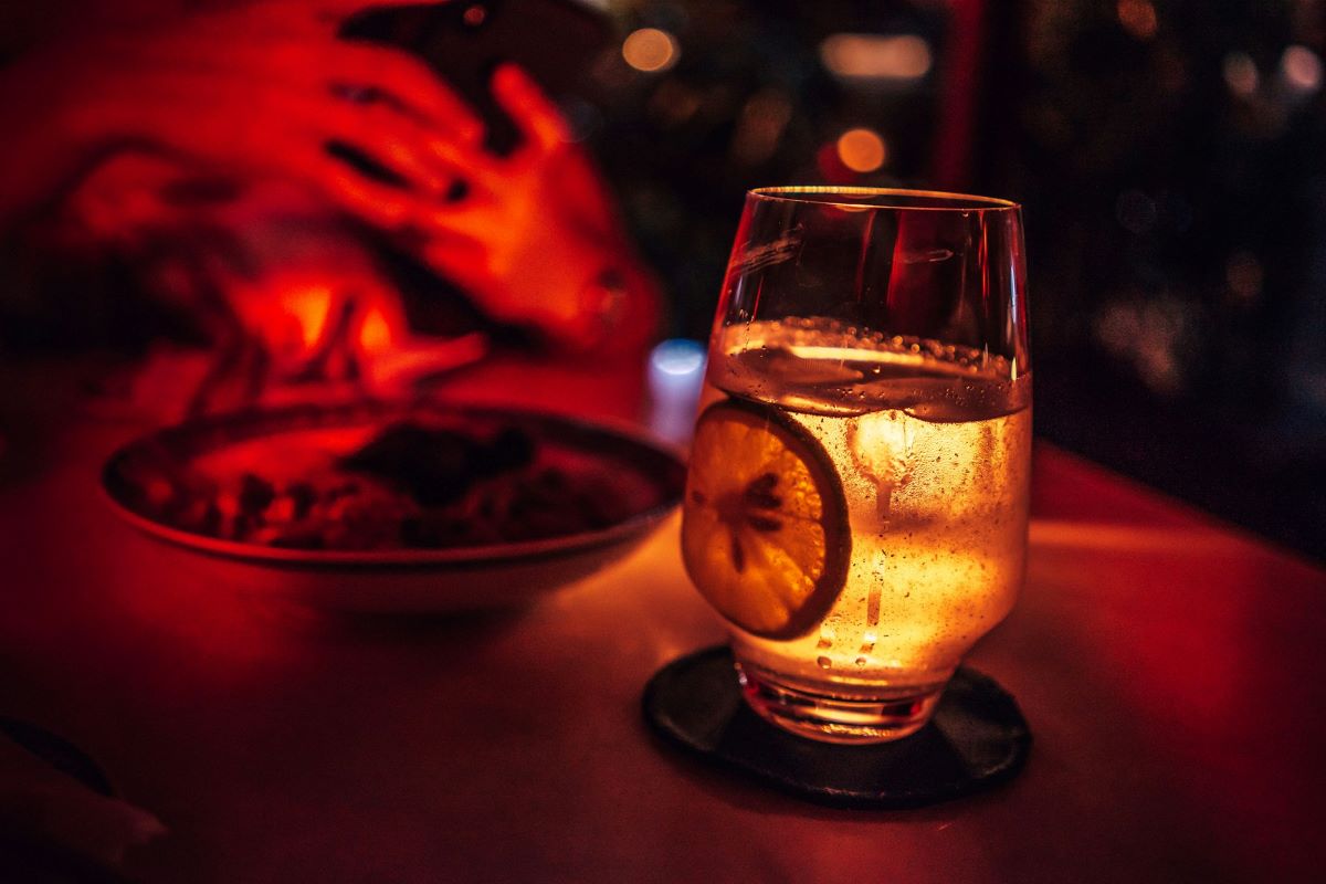 A woman taking a picture of a cocktail inside a dark club. 