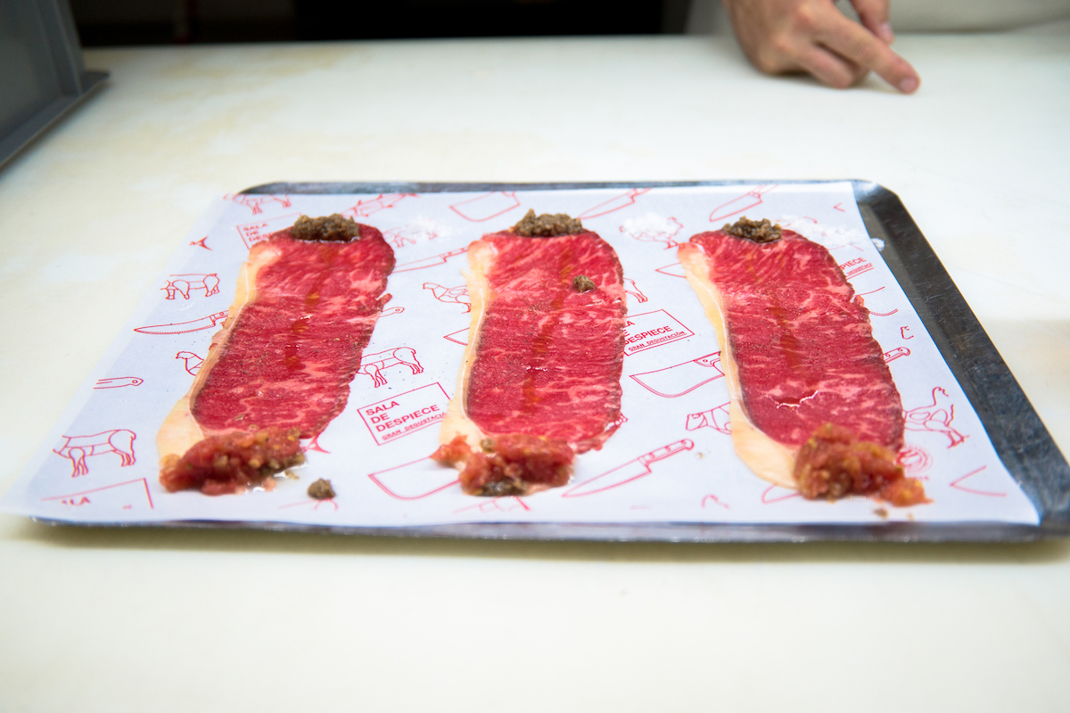 Three slices of meat cut very thin on a white tray with bits of sauce and seasoning at either end.