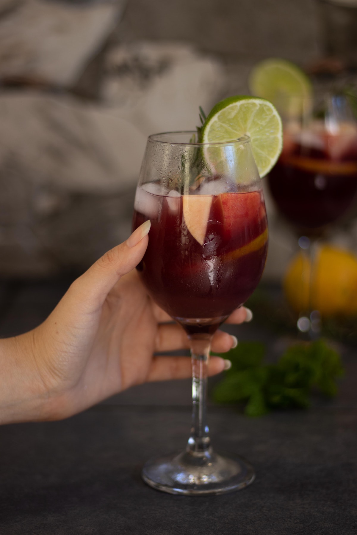 Person's hand holding a wine glass of sangria garnished with fruit and fresh herbs enjoying lunch in Madrid. 