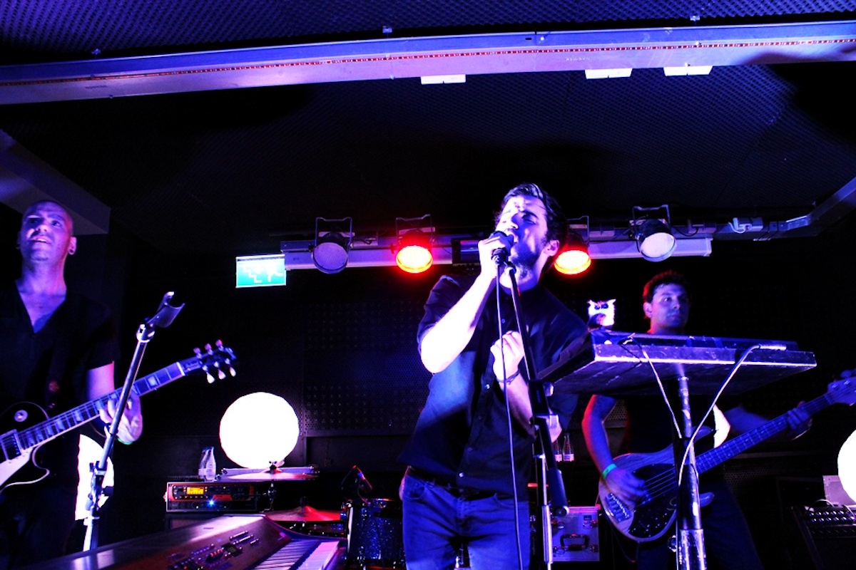 A rock band performs on a stage with purple lighting.