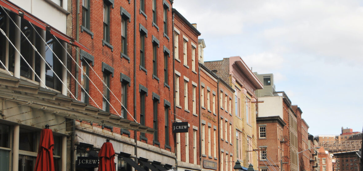 Multi-story historic buildings lining a pedestrian street with several cafe tables in front of them