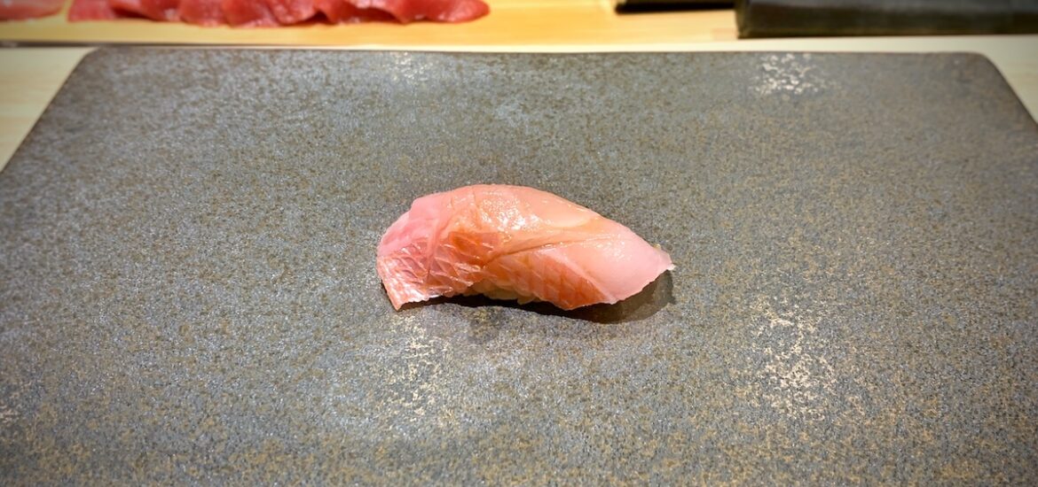 Small piece of pink sushi on a gray square plate.