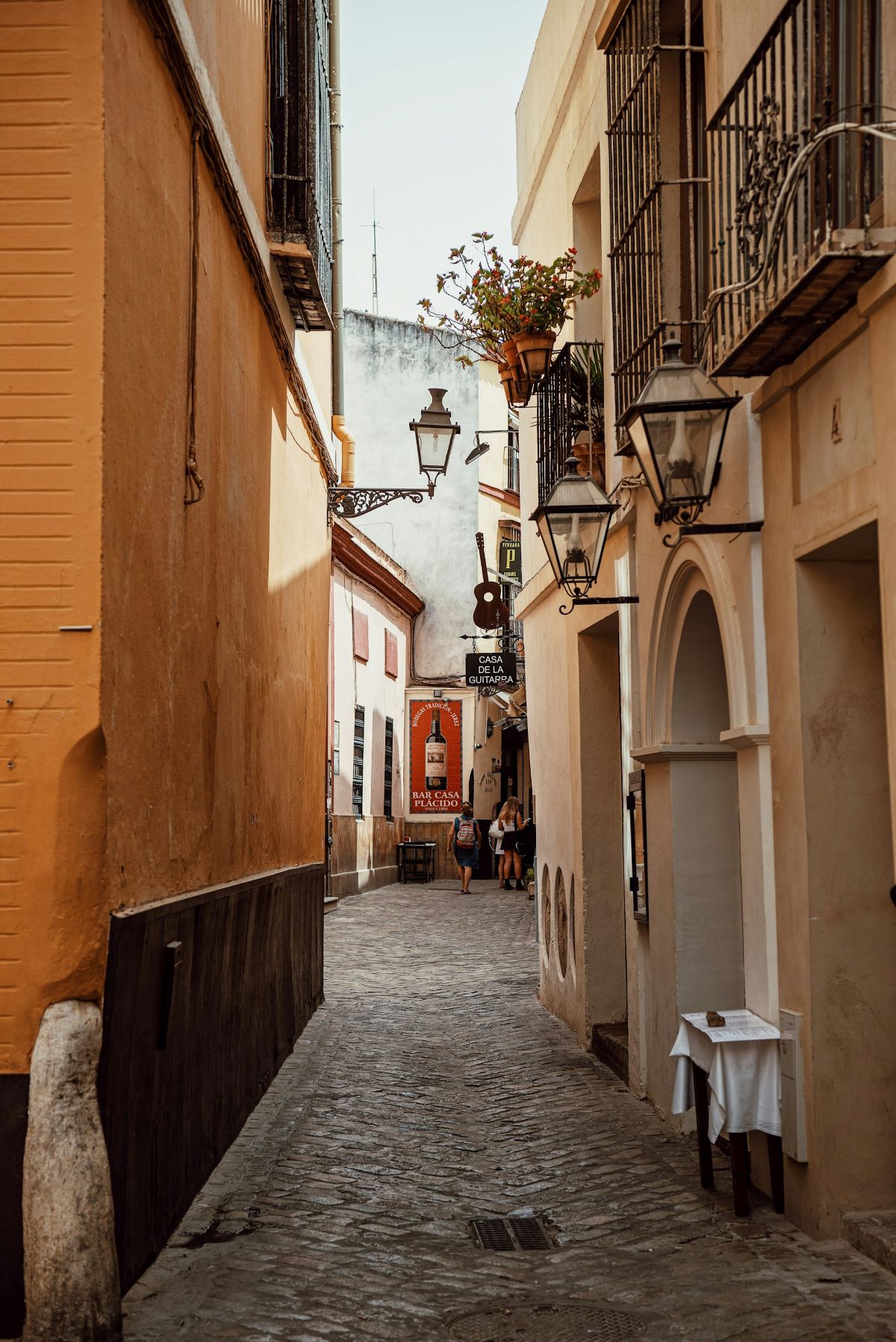 People walking down the narrow streets of Barrio Santa Cruz finding where to keep cool in Seville. 