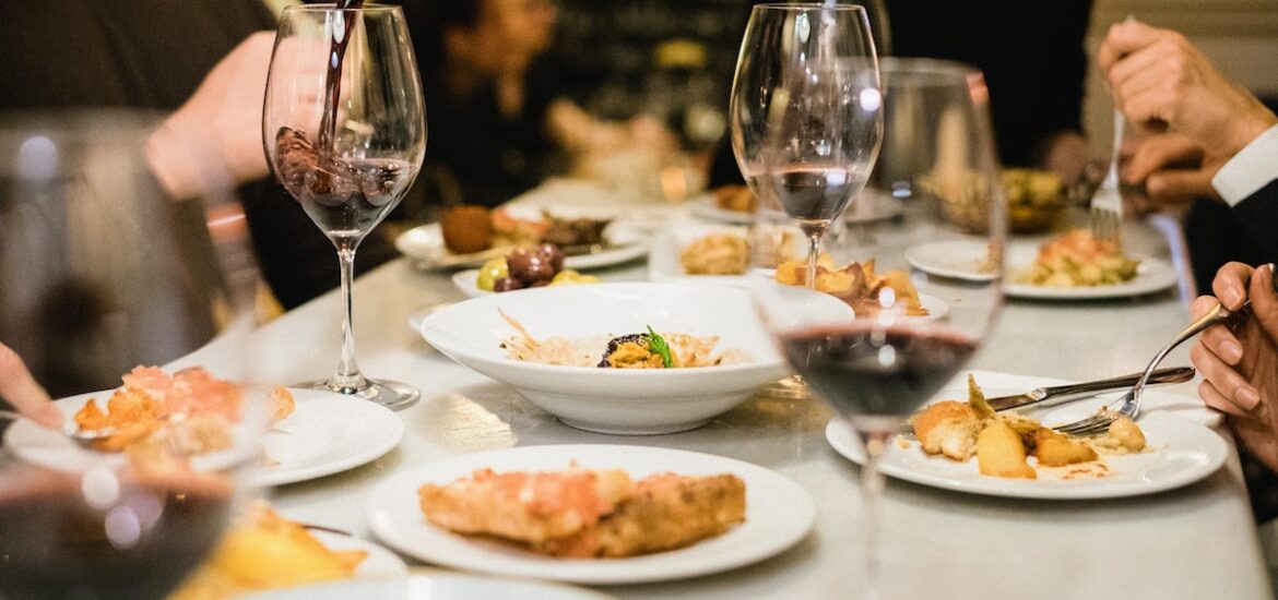 Table full of multiple small tapas plates and glasses of red wine.