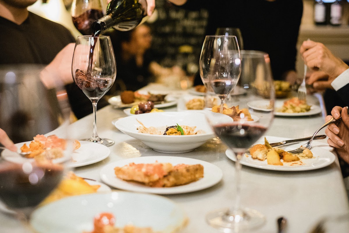 Table full of multiple small tapas plates and glasses of red wine.