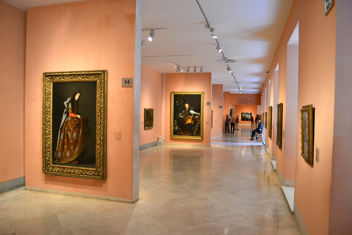 Paintings hanging on coral-colored walls at the Thyssen Museum in Madrid.