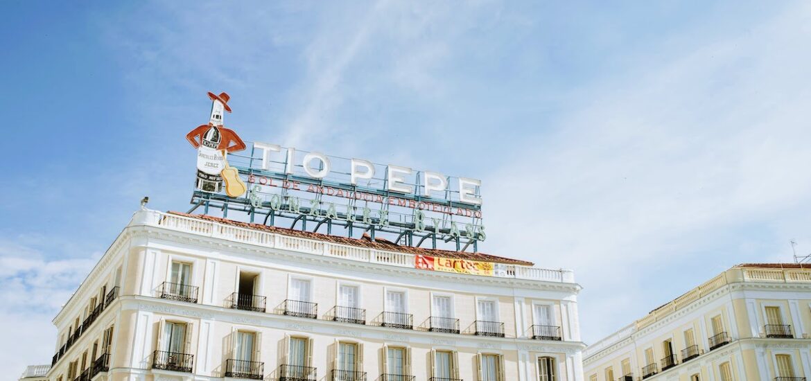 White building on a clear day with a neon advertising sign for sherry wine atop the roof.