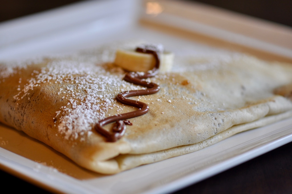 Close-up of folded Parisian crepe drizzled with chocolate, powdered sugar, and banana slices