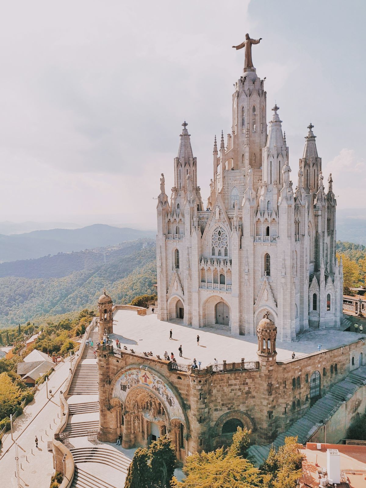 Arial view of a large white church on a hill with a statue on the top of the building.