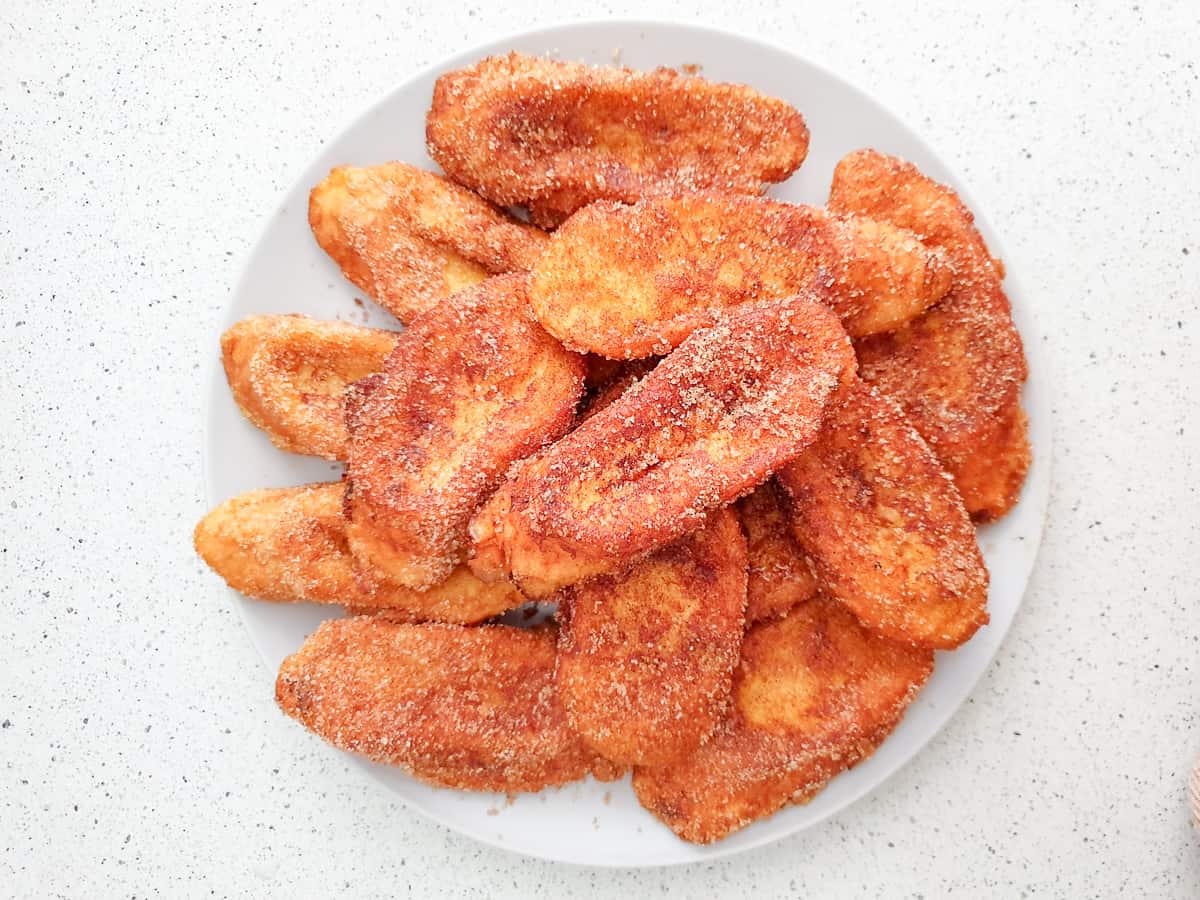 Overhead shot of fried bread slices sprinkled with cinnamon sugar on a white plate