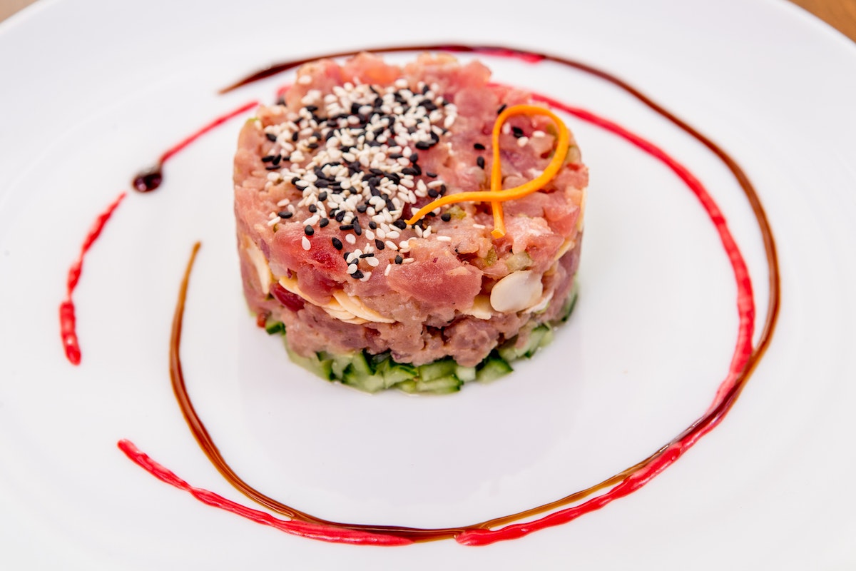 Tuna tartare surrounded by rings of red sauce on a white plate