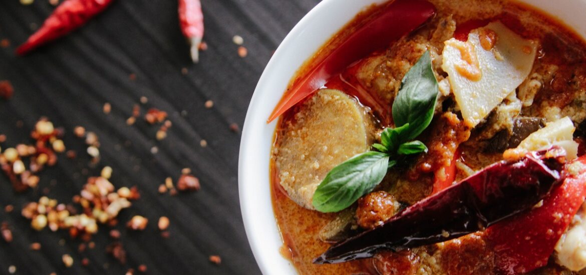 Bowl of watery red curry with chilis and chili flakes