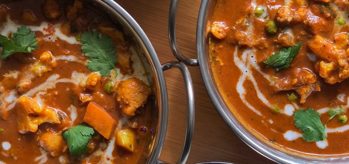 Two small bowls of white rice and two dishes with cauliflower in a brown sauce, all garnished with herbs