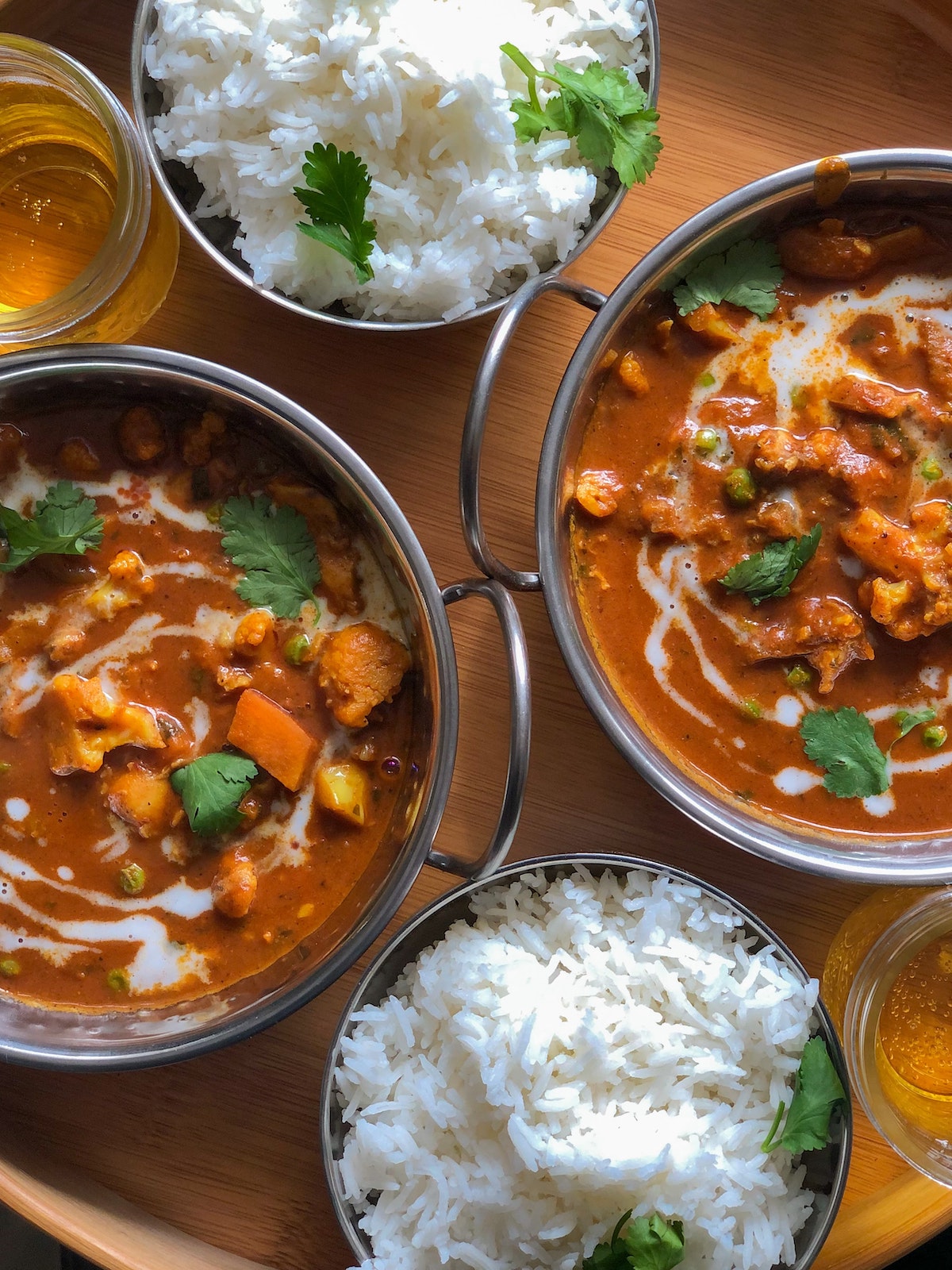 Two small bowls of white rice and two dishes with cauliflower in a brown sauce, all garnished with herbs