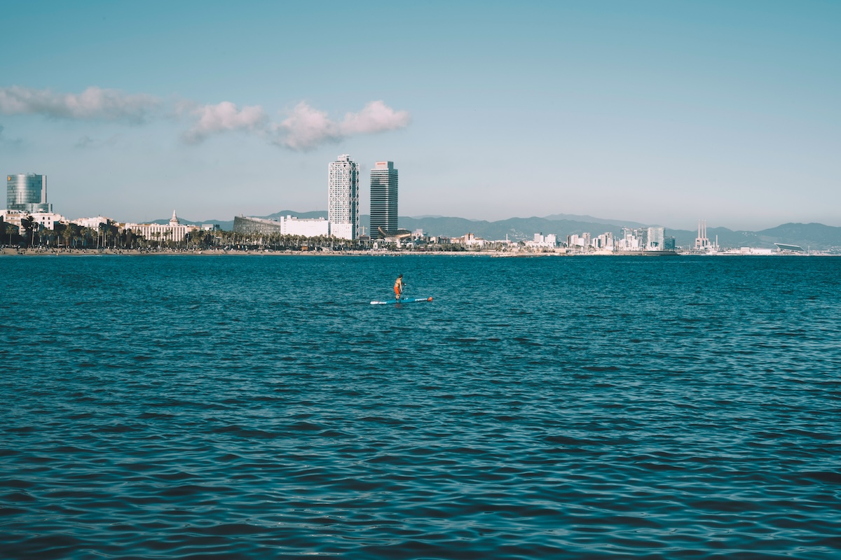 man paddle boarding on the sea with the city of barcelona in the background