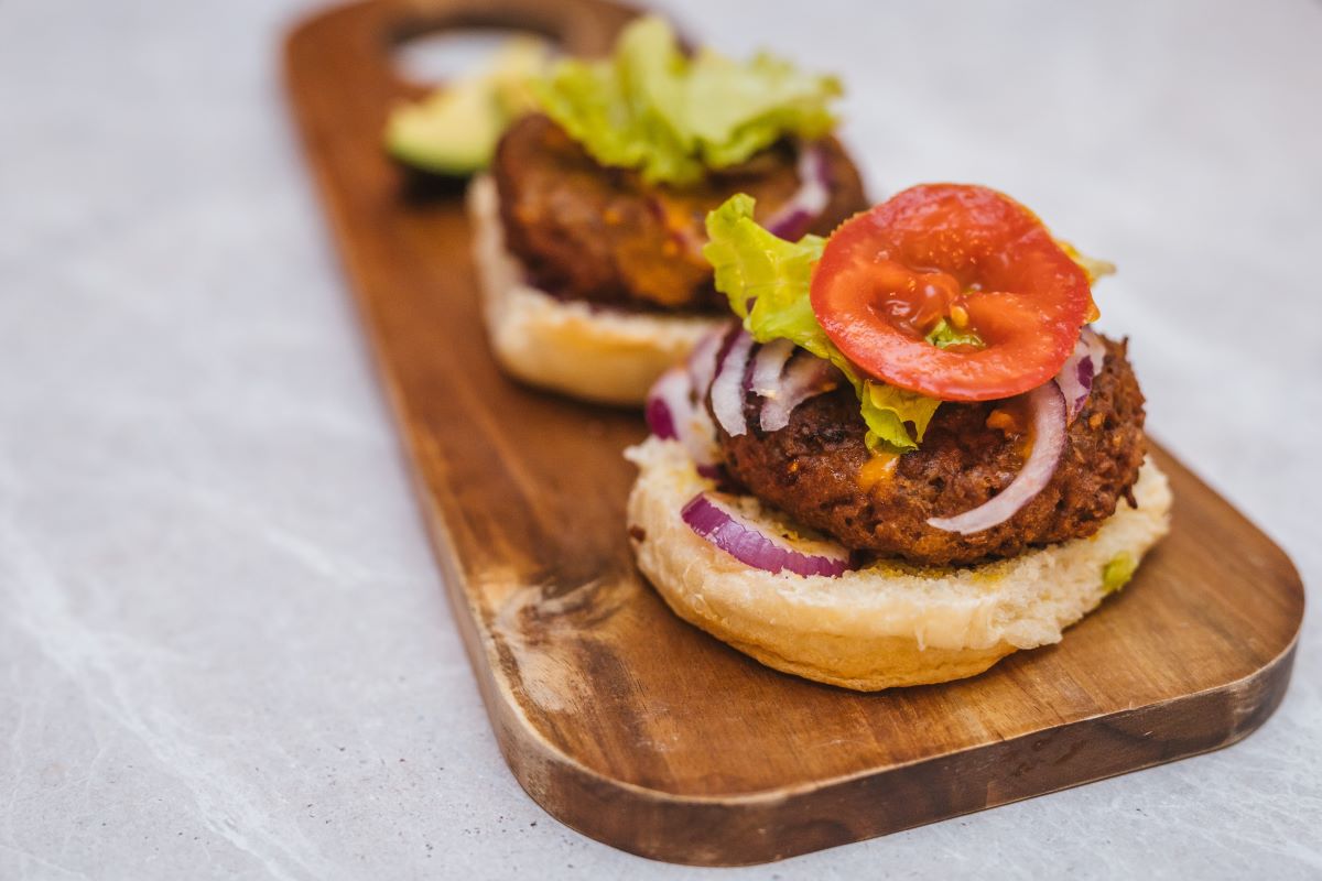 A veggie burger, open faced, displaying its toppings including tomato, red onion, lettuce and avocado