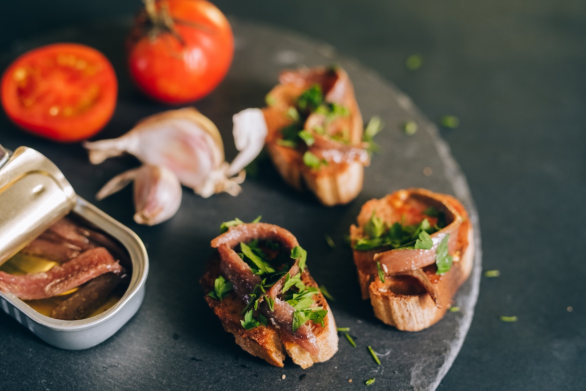 A can of anchovies with small pieces of toast with anchovies, garlic, garlic and tomatoes.