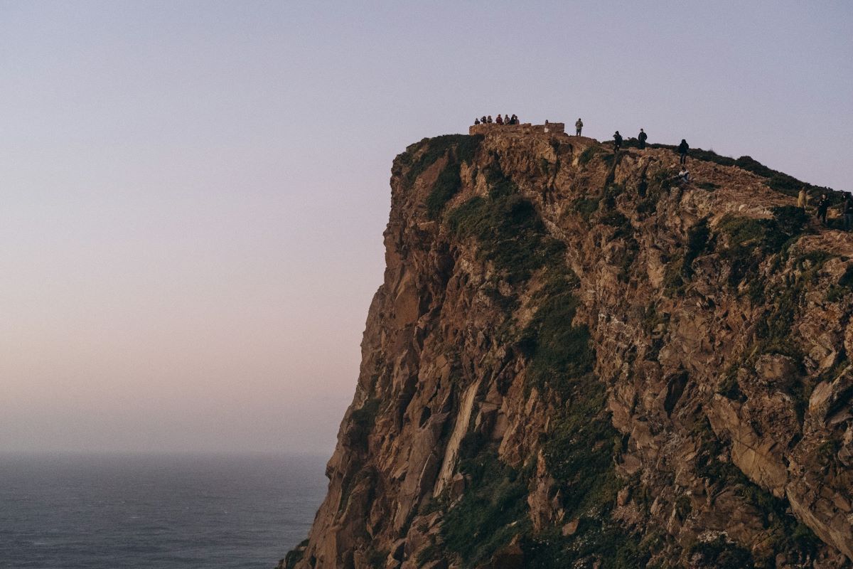 A tall cliff with people at the top taking in the views. 