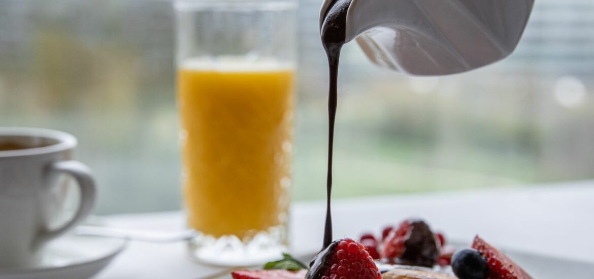 A plate of pancakes being drizzled with chocolate sauce.